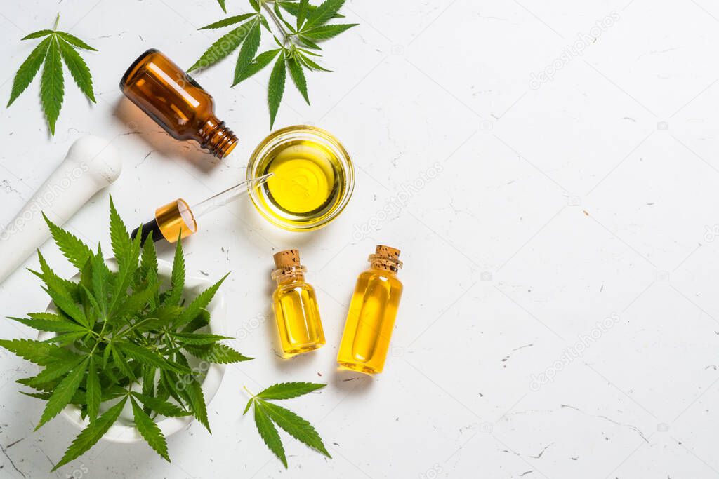 Cannabis oil in glass bottles and cannabis leaves at white table.