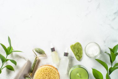 Yeşim silindir ve gua sha taş masaj aleti. Yüz kremi ve serum şişesiyle..