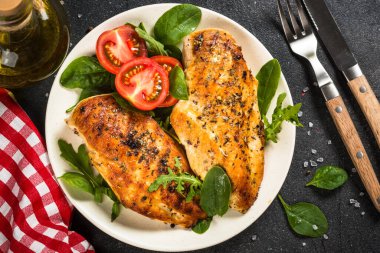 Siyah arka planda beyaz tabakta ızgara tavuk filetosu..