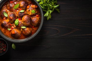 Karanlık taş masada bir tavada domates soslu köfte.