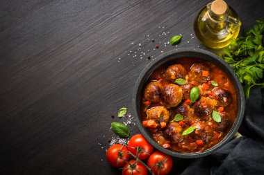 Karanlık taş masada bir tavada domates soslu köfte.