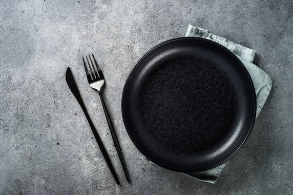 Assiette noire avec couverts à table en pierre grise. — Photo