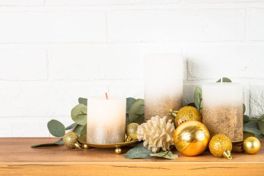 Kapalı mekanda Noel süslemeleri - Mumlu raflar, okaliptüs dalları ve altın dekorlar.