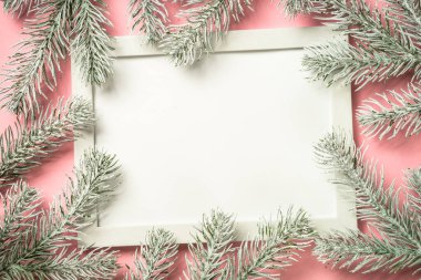 Fotoğraf çerçeveli Noel kompozisyonu ve pembe arka planda köknar ağacı dalı.