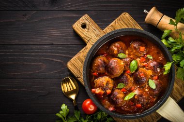 Koyu ahşap masada tavada domates soslu köfte. Düz görünüm.