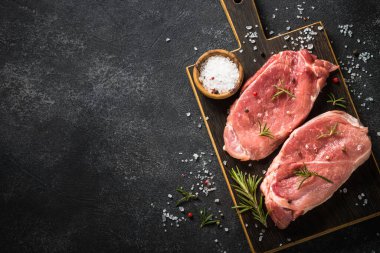 Siyah arka planda baharatlı ve otlu taze biftekler.