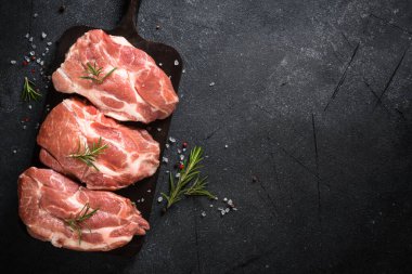 Siyah arka planda baharatlı ve otlu taze biftekler.