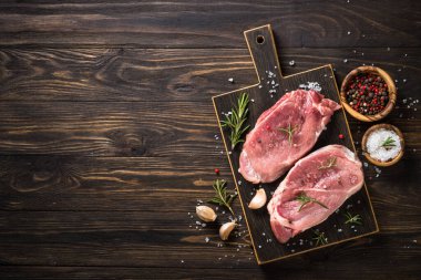 Siyah arka planda baharatlı ve otlu taze biftekler.