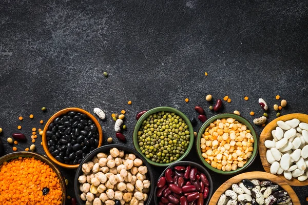 Surtido de legumbres, lentejas, garbanzos y frijoles sobre mesa de piedra negra. — Foto de Stock