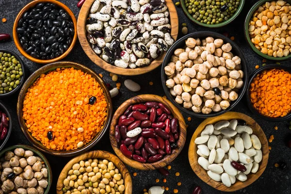 Surtido de legumbres, lentejas, garbanzos y frijoles sobre mesa de piedra negra. — Foto de Stock