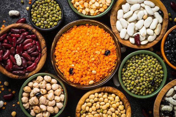 Surtido de legumbres, lentejas, garbanzos y frijoles sobre mesa de piedra negra. — Foto de Stock