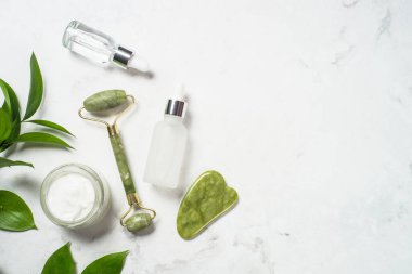 Yeşim silindir ve gua sha taş masaj aleti. Yüz kremi ve serum şişesiyle..