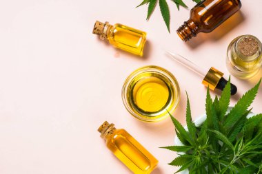 Cam şişelerde esrar yağı ve beyaz masada esrar yaprakları.