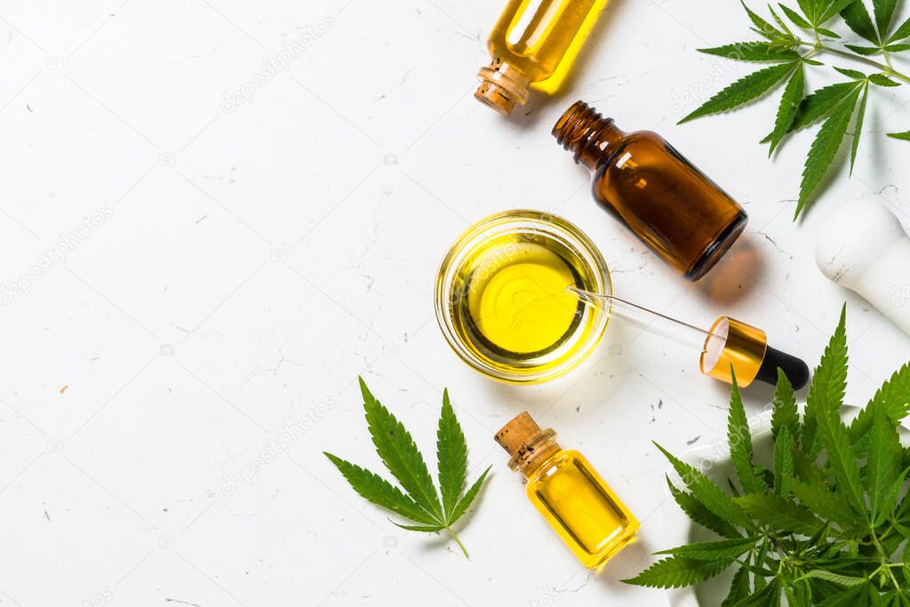 CBD oil in glass bottles and cannabis leaves at white table.