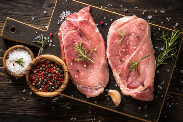 Fresh steaks with herbs and spices at wooden table. — Stock Photo, Image