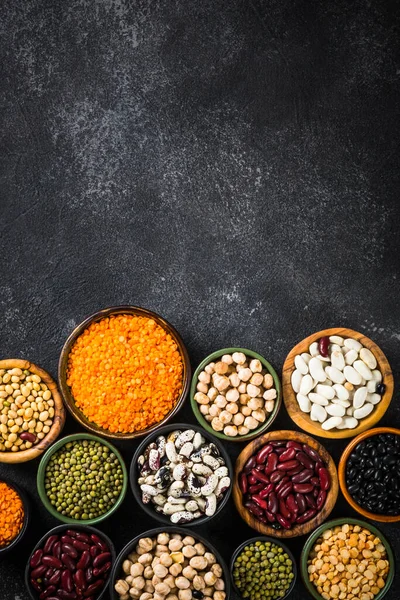 Surtido de legumbres, lentejas, garbanzos y frijoles sobre mesa de piedra negra. — Foto de Stock