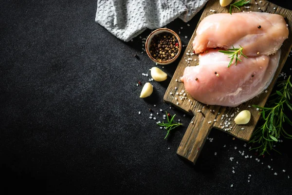 Baharatlı tavuk filetosu ve siyah taş masadaki tahta tahtada otlar..