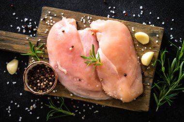 Baharatlı tavuk filetosu ve siyah taş masadaki tahta tahtada otlar..