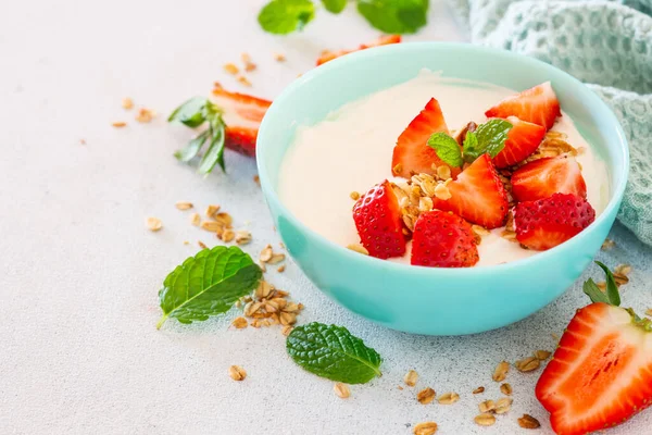 Yogurt with granola and strawberry in white bowl at light stone table. — Stock Photo, Image