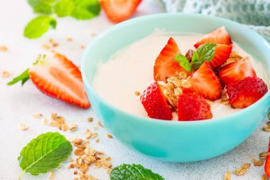 Yoğurtlu granola ve çilekli beyaz kâse, hafif taş masada..