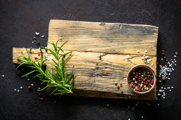 Gammal skärbräda, örter och kryddor vid mörkt köksbord. — Stockfoto