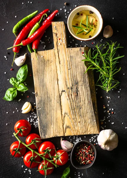 Food background. Oak cutting board, spices and vegetables at kitchen table. — Foto de Stock