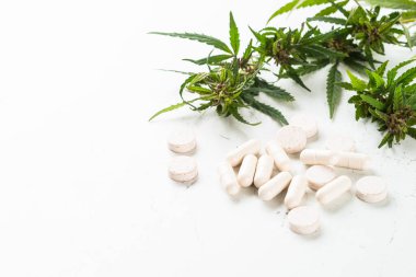 Cam şişelerde CBD yağı ve beyaz masada kenevir yaprakları.