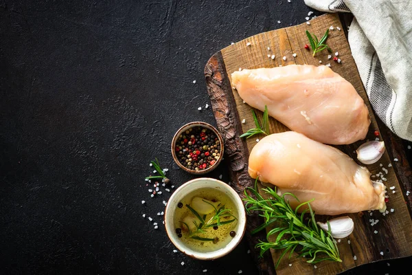 Kippenfilet borst met specerijen en kruiden aan houten plank aan zwarte tafel. — Stockfoto