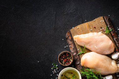 Baharatlı tavuk fileto göğsü ve siyah masada ahşap tahtada otlar..