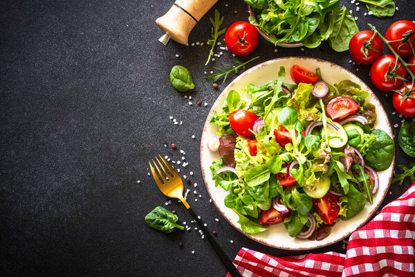 Green salad, Fresh salad leaves and vegetables at black background.