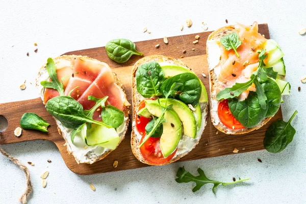 Open sandwich set with cream cheese, prosciutto, salmon, avocado and fresh greens. — Stockfoto