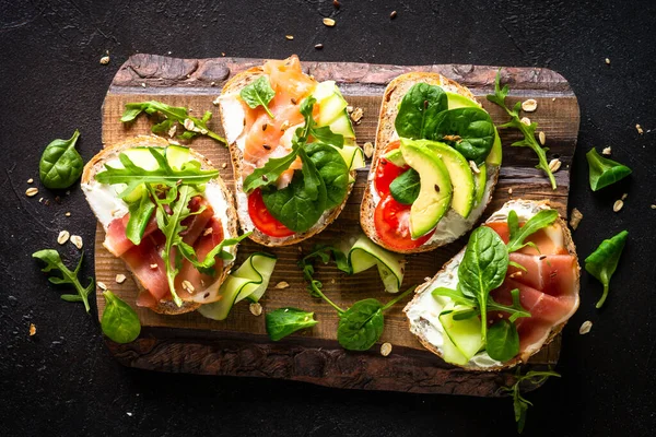 Open sandwich set with cream cheese, prosciutto, salmon, avocado and fresh greens. — Stockfoto