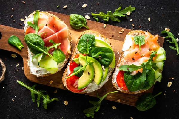 Open sandwich set with cream cheese, prosciutto, salmon, avocado and fresh greens. — Stockfoto