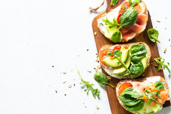 Open sandwich set with cream cheese, prosciutto, salmon, avocado and fresh greens. — Stockfoto