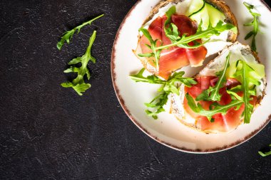 Krem peynirli sandviç ve roka soslu beyaz tabak. Koyu masadaki üst görünüm.