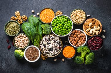 Vegan protein kaynağı. Baklagiller, fasulyeler, fındıklar, sebzeler ve tohumlar. Siyah taş masadaki en üst manzara. Sağlıklı vejetaryen yemekleri.