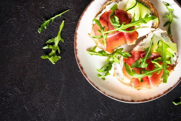 Krem peynirli sandviç ve roka soslu beyaz tabak. Koyu masadaki üst görünüm.