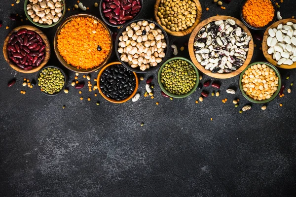 Baklagil, mercimek, bezelye ve fasulye çeşitleri siyah taş masadaki farklı kaselerde. Dizayn için alanı olan düz resim.