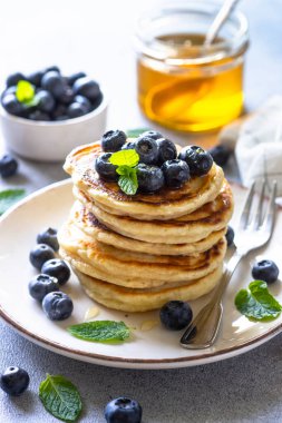 Beyaz taş masada taze yaban mersinli krep ve bal yığını..