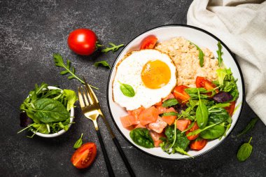 Tuzlu kahvaltı. Tuzlu somon, yumurta ve taze salatalı yulaf ezmesi. Siyah masadaki üst görünüm.