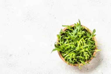 Arugula taze yeşil yapraklar beyaz masada kasede.