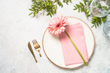 Beyaz tabak, pembe çiçek ve çatal bıçak takımları beyaz mutfak masasında. Kopyalama alanı olan üst görünüm.