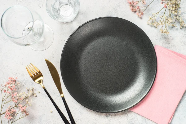 Beyaz mutfak masasında siyah tabak, çiçekler ve çatal bıçak takımı. Tasarım için alanı olan üst görünüm.