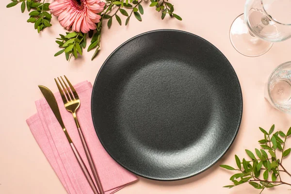 Tabaklar, bardaklar, çatal bıçaklar ve çiçekler pembe arka planda. Kopyalama alanı olan üst görünüm.