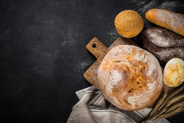 Siyah masada taze ekmek, beyaz çavdar ve çörekler. En üst görüntü.