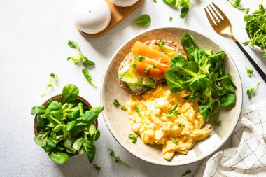 Çırpılmış yumurta, krem peynirli sandviç, somon balığı ve beyaz taş masada salata yaprakları. Kopyalama alanı olan üst görünüm.