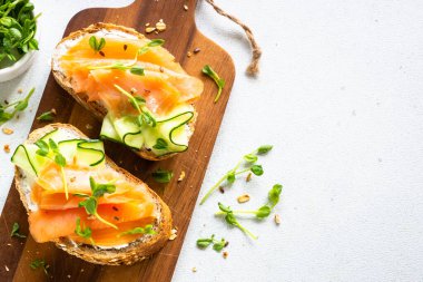 Krem peynirli, somonlu ve salatalıklı sandviç. Beyaz masadaki üst görünüm.