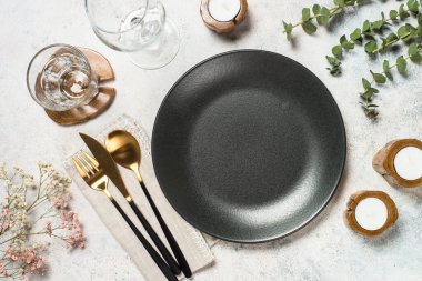 Beyaz mutfak masasında siyah tabak, yeşil yapraklar, çiçekler ve çatal bıçak takımı. Üst görünüm.