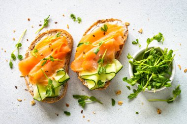 Krem peynirli, somonlu ve salatalıklı sandviç. Beyaz masadaki üst görünüm.