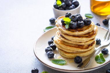 Beyaz taş masada taze yaban mersinli krep ve bal yığını..